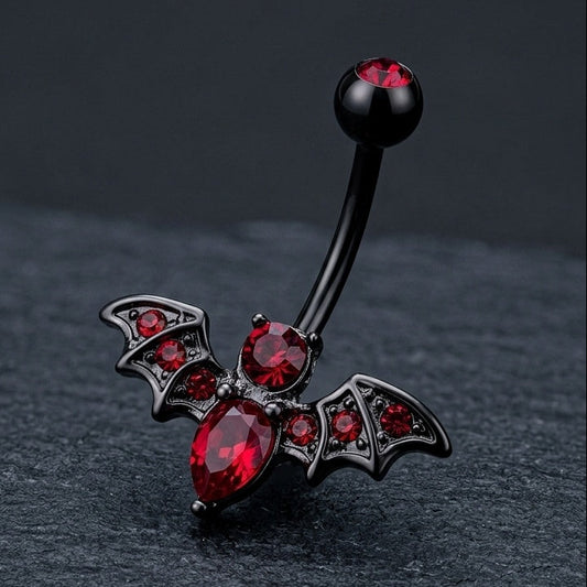 Belly button ring with bat design and red gemstones on a dark background.