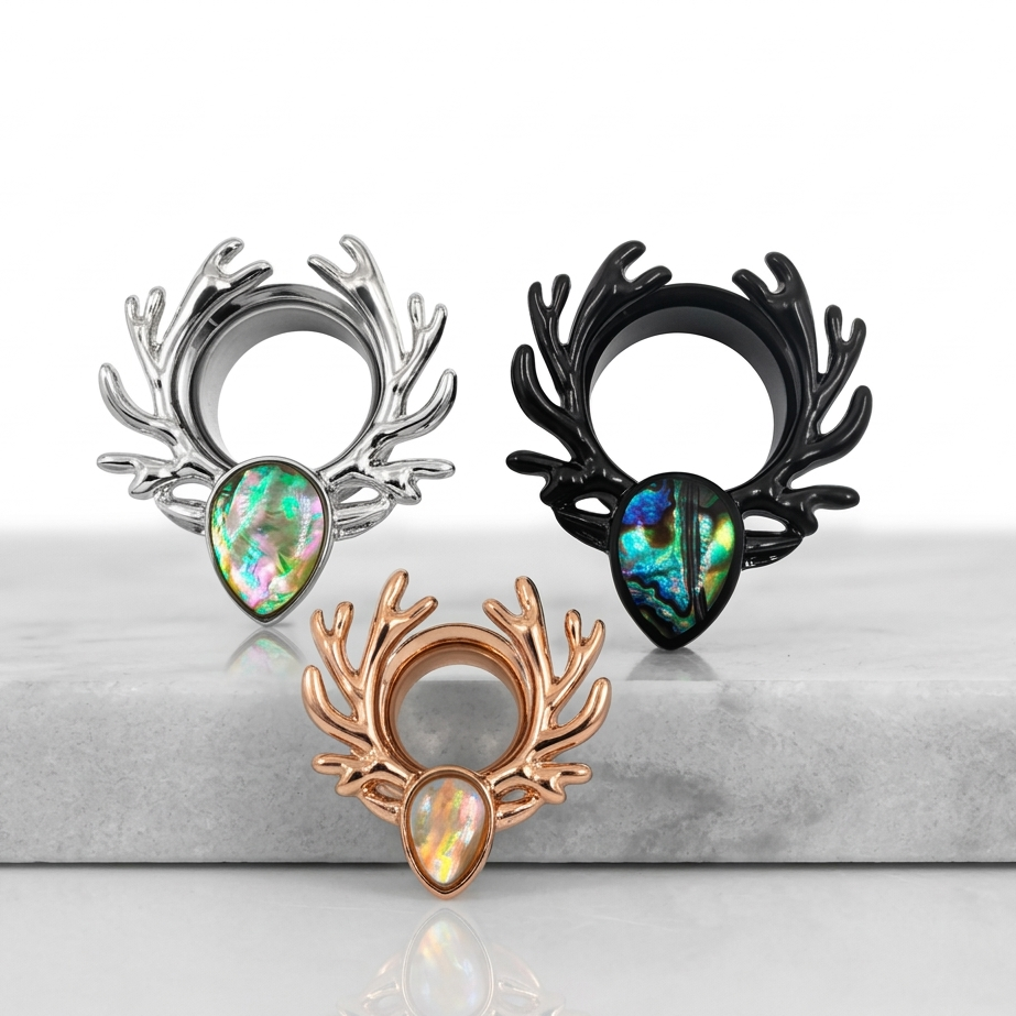 Three decorative antler-shaped objects with gemstones on a reflective surface.