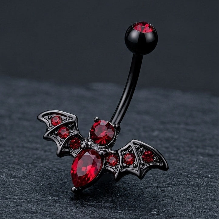 Belly button ring with bat design and red gemstones on a dark background.