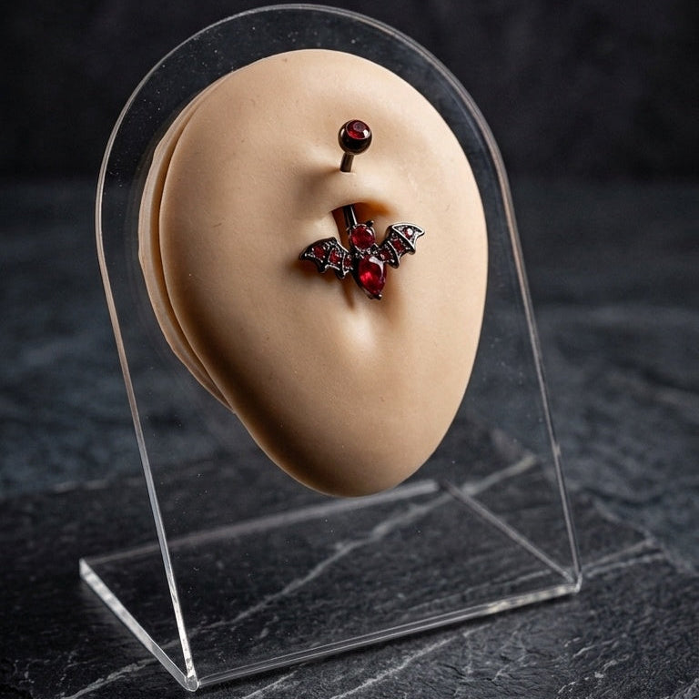 Red and black vampire bat belly bar displayed on a piercing jewellery stand.