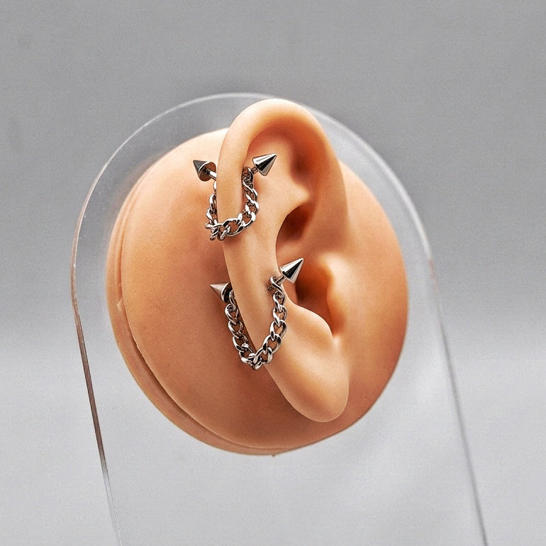 Ear with silver earrings on a clear stand against a gray background
