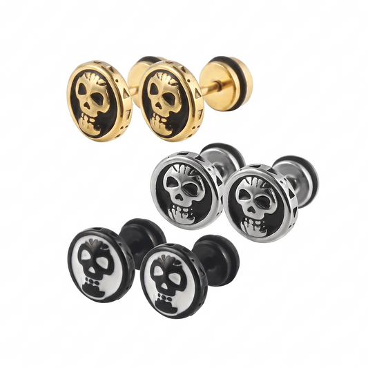 Three pairs of round stud earrings with skull motifs, shown on a plain white background: one pair in gold-tone with black enamel, one pair in silver-tone with black enamel, and one pair in black with white enamel.